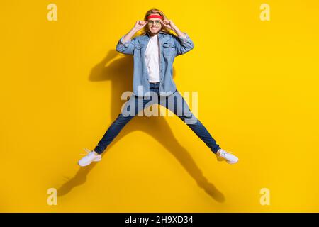 Photo de joli jeune gars habillé denim chemise souriant bras sombre lunettes sautant haut isolé couleur jaune fond Banque D'Images