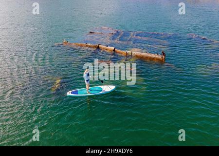 Femme sur le paddle board, sup à côté de l'épave abandonnée brisée qui colle de la mer Banque D'Images