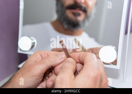 Homme à barbe caucasien mature qui dépose ses ongles de main devant un miroir Banque D'Images