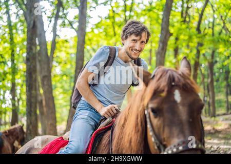 un bel homme se balade sur le cheval noir dans la forêt verte Banque D'Images