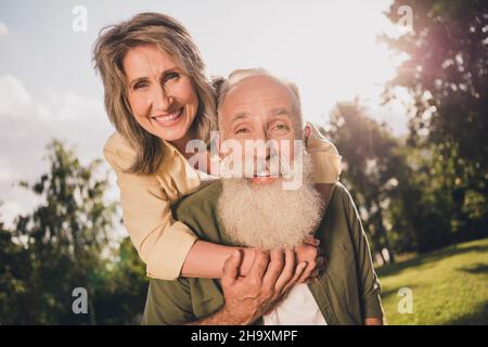 Photo d'un couple d'âge charmant pigeyback porter une chemise marcher dans le parc à l'extérieur Banque D'Images
