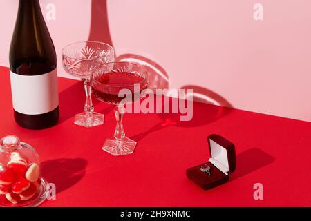 Proposition de mariage Saint Valentin concept.Anneau, vin mousseux, verres et bonbons sur table rouge Banque D'Images