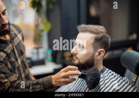Le maître enlève les cheveux restants du client à l'aide d'une brosse Banque D'Images