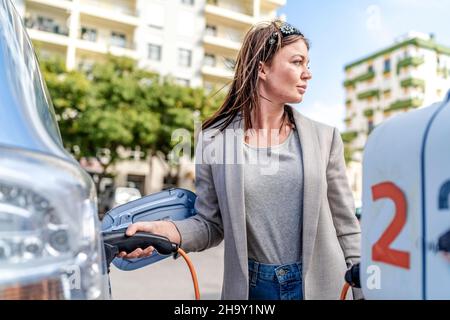 Femme en charge d'une voiture électrique en milieu urbain, Faro, Portugal Banque D'Images