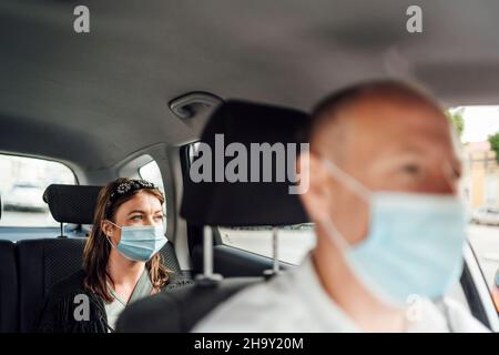 Chauffeur de taxi dans un masque avec une cliente sur le siège arrière portant un masque Banque D'Images