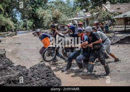 Kamar Kajang, Indonésie.09th décembre 2021.Les villageois évacuent une moto qui se trouvait dans les cendres après l'éruption du mont Semeru dans les villages de Kamar Kajang, à Lumajang.Au moins 14 personnes sont mortes et des dizaines sont blessées après que le mont Semeru, un volcan de la province de Java est en Indonésie, a éclaté samedi, lançant des tours de cendres et des nuages chauds qui couvraient les villages voisins.Crédit : SOPA Images Limited/Alamy Live News Banque D'Images