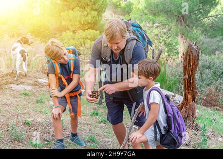 Moniteur de scout de garçon avec deux jeunes randonneurs enfants et leur chien de compagnie compagnon au milieu de la forêt.Le moniteur leur explique les concepts de la nature Banque D'Images