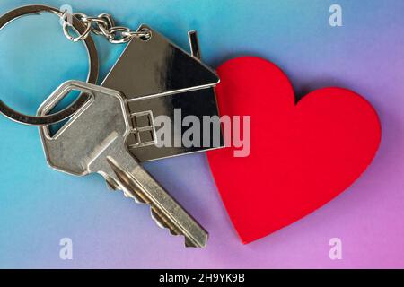 Clé avec charme en forme de coeur et petite maison sur fond violet pastel et rose vue de dessus avec espace copie, nouvelle maison et concept immobilier Banque D'Images