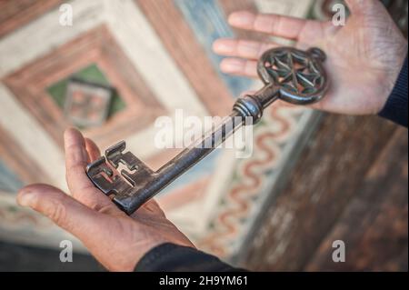 Gros plan vue de détail des mains humaines tient vieux grand énorme clé en métal énorme pour l'entrée de l'église.Secret et mystère.Sécurité médiévale Banque D'Images