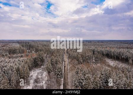 Panorama hivernal idyllique depuis une vue aérienne avec une forêt enneigée et une route menant à l'horizon. Banque D'Images