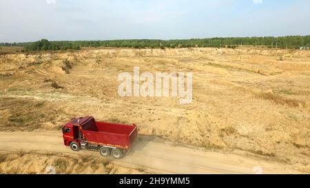 Décharger le camion sur la route rurale.Scène.Vue de dessus des trajets en camion, laissant des panaches de poussière dans la route de terre en campagne, dans le contexte de la carrière de pelle hydraulique Banque D'Images