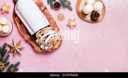 Bordure avec gâteau de Noël Stollen, branches d'arbre et décor doré sur table rose clair.Banderole de Noël, sapin et cornets de pin doré, Banque D'Images