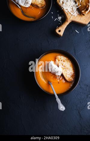 Soupe crémeuse de noyer cendré à la crème, toasts de parmesan dans un bol en céramique brune sur fond gris foncé, plat végétarien confortable à l'automne Banque D'Images
