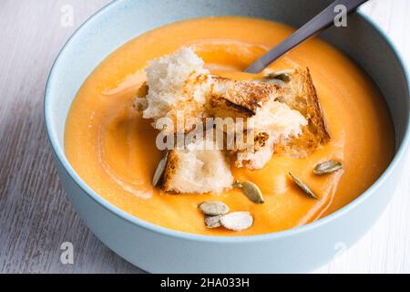 Soupe de courge musquée crémeuse avec pain grillé croûtons dans un bol en céramique bleue sur fond de bois blanc, plat végétalien confortable d'automne Banque D'Images