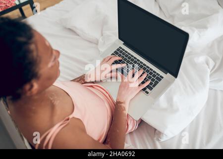 Une femme assise au lit et travaillant sur un ordinateur portable Banque D'Images