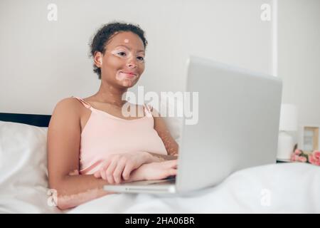 Une femme assise au lit et travaillant sur un ordinateur portable Banque D'Images