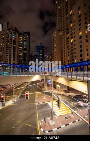 Vue nocturne d'un très grand pont piétonnier sur une route principale dans le quartier de la Marina de Dubaï, Dubaï, Émirats arabes Unis, entouré de gratte-ciels Banque D'Images