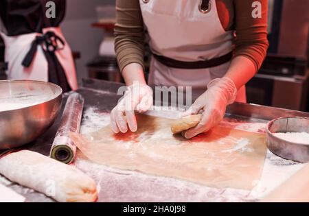 une femme chef travaille avec une pâte dans la cuisine dans un restaurant proche de ses mains. préparation de pizza Banque D'Images