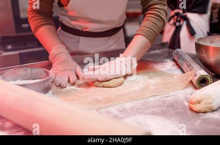 une femme chef travaille avec une pâte dans la cuisine dans un restaurant proche de ses mains. préparation de pizza Banque D'Images