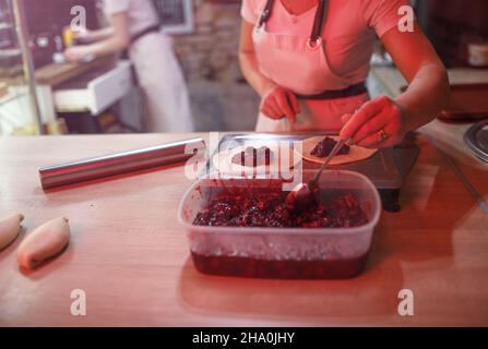 le cuisinier de fille met la cerise remplir des tartes.Préparation de desserts sucrés. Cuisine ouverte dans la boulangerie. Banque D'Images