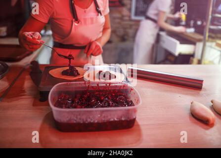 le cuisinier de fille met la cerise remplir des tartes.Préparation de desserts sucrés. Cuisine ouverte dans la boulangerie. Banque D'Images