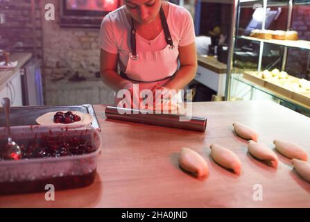 la fille est un cuisinier dans la cuisine enveloppant des tartes avec remplissage de cerise. cuisine ouverte dans la boulangerie Banque D'Images