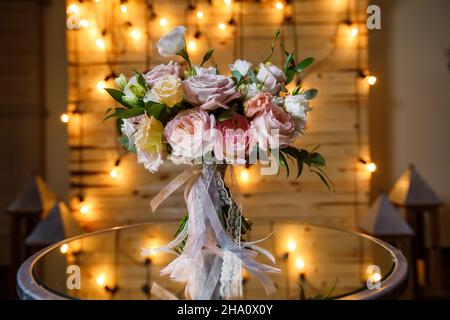 Délicat et très beau bouquet de mariage de roses, verdure, eustoma debout sur table miroir.Fleurs de mariée tendance dans des tons pastel sur le fond des ampoules d'éclairage de soirée Banque D'Images