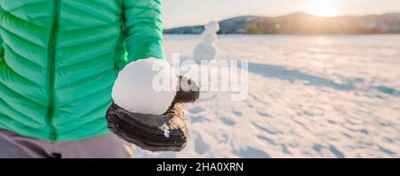 Hiver Snowball combat concept en plein air.Fille tenant boule de neige le jour de neige avec bonhomme de neige en arrière-plan sur le lac gelé à beau coucher de soleil d'hiver vie Banque D'Images