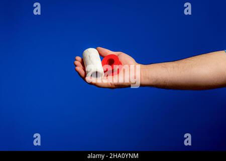 Main de l'homme offrant sur sa paume un bandage et un rouleau de ruban.Équipement de base pour toutes les plaies.Isolé sur fond de studio bleu Banque D'Images