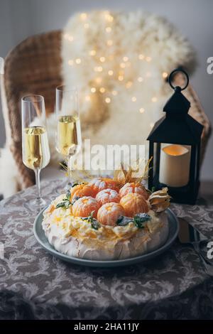 Dessert à base de meringue au gâteau Pavlova nommé d'après la ballerine russe décorée de mandarines fraîches, de caramel, de physalis et de sucre en poudre avec deux champa Banque D'Images