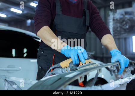 Réparation de la carrosserie de voiture par le ficelage de gros travaux après l'accident en travaillant le primaire de ponçage avant la peinture., le mécanicien répare la voiture , en utilisant Banque D'Images