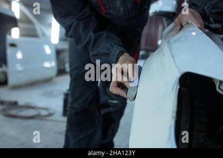 Réparation de la carrosserie de voiture par le ficelage de gros travaux après l'accident en travaillant le primaire de ponçage avant la peinture., le mécanicien répare la voiture , en utilisant Banque D'Images