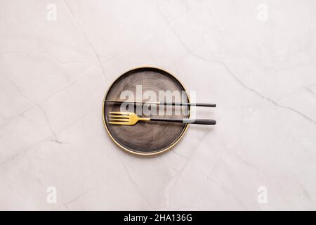 Vue de dessus image d'une assiette en métal d'époque avec des couverts dorés et des poignées noires sur une table en marbre blanc Banque D'Images