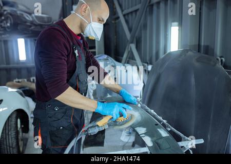 Ponçage d'une partie de carrosserie de voiture avec une rectifieuse électrique avant peinture, service de réparation de carrosserie de véhicule. Banque D'Images