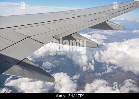 Vue depuis la fenêtre passager de l'avion commercial, nuages sur ciel bleu visibles sous l'aile de l'avion Banque D'Images
