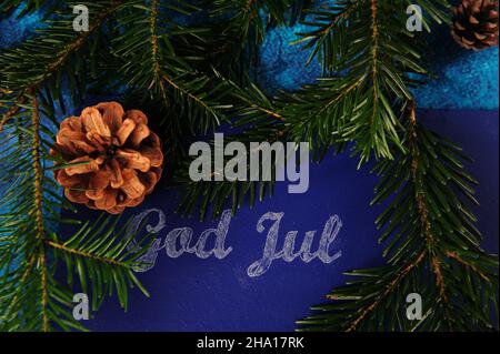 Brindilles et pinecones d'épinette entourant les mots dieu jul écrit en craie sur tableau noir bleu.Vœux de Noël norvégien. Banque D'Images