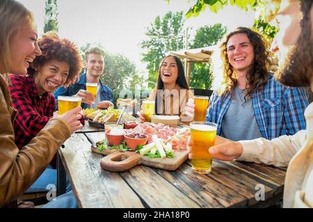 Groupe d'amis heureux multiethniques vivant un style de vie sain et souriant et en train de se délecler tout en buvant de la bière au restaurant de pub extérieur Banque D'Images