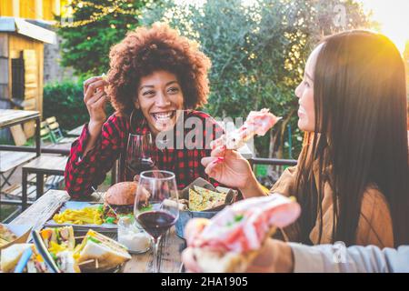 Groupe d'amis multiethniques vivant un style de vie sain et souriant et plaisantant tout en buvant du vin rouge au restaurant de pub extérieur Banque D'Images