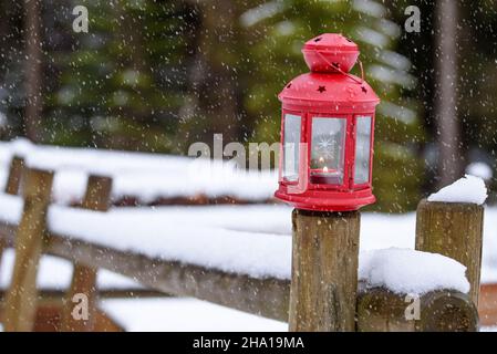 Gros plan d'une lanterne de Noël éclairée sur une clôture en bois en plein air lors d'une journée d'hiver en neige.Décorations de Noël. Banque D'Images