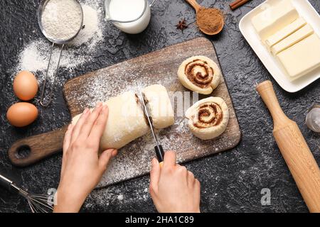 Femme préparant des rouleaux de cannelle sur fond noir Banque D'Images