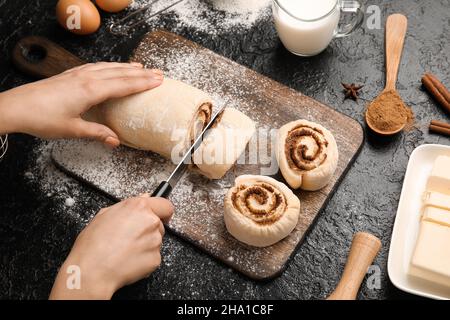 Femme préparant des rouleaux de cannelle sur fond noir Banque D'Images