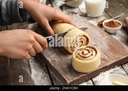 Femme préparant de savoureux petits pains à la cannelle sur fond de bois Banque D'Images