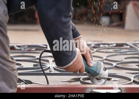 Homme meule une clôture en métal avec une meuleuse d'angle.Gros plan des mains et des outils.Vue latérale Banque D'Images
