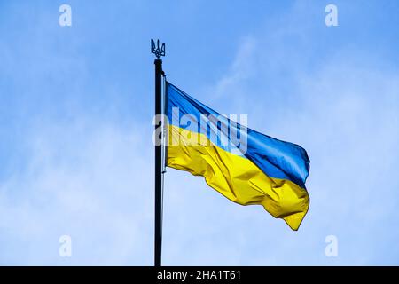 Drapeau ukrainien dans les rayons du soleil levant sur fond de ciel. Drapeau national bicolore bleu et jaune de l'Ukraine sur un mât et un blason Banque D'Images