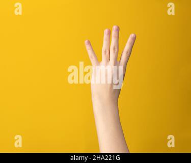 Geste de main femelle sur fond jaune.Femme isolée à la main montrant l'index, le milieu, l'anneau et les quatre petits doigts. Banque D'Images