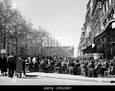 Café-terrasse le long des champs-Élysées avec l'Arc de Triomphe en arrière-plan, 1945.L'une des deux photos qui représentent le même café-terrasse situé peut-être près du métro George V.Il est bondé à la capacité et beaucoup de clients sont clairement des militaires américains ou britanniques.C'est un jour ensoleillé et les arbres affichent le feuillage du début du printemps.Il y a beaucoup de piétons dans la rue.L'humeur est ce que vous vous attendriez pour un beau jour de printemps avec l'occupation un souvenir récent.L'Arc de Triomphe est en arrière-plan. Banque D'Images