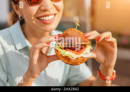 Bonne jeune femme asiatique mangeant un délicieux hamburger fastfood dans le restaurant de la rue Banque D'Images