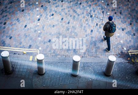 Un piéton traverse la route à l'extérieur de la gare de St Pancras à Kings Cross, Londres, Royaume-Uni.Vu du dessus, vous pouvez voir les bornes de sécurité, les bandes de grondement, le pavage de blocs et les lignes jaunes. Banque D'Images