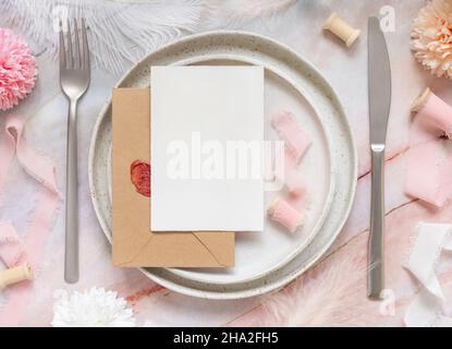 Table de mariage place avec une carte en papier sur enveloppe scellée près des fleurs, des rubans de soie et des plumes vue du dessus.Modèle romantique avec blanc horizontal Banque D'Images