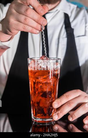 La main d'un barman professionnel agite le sirop rouge dans un cocktail alcoolisé avec une cuillère de bar sur le comptoir du bar.Le processus de préparation d'une alc Banque D'Images